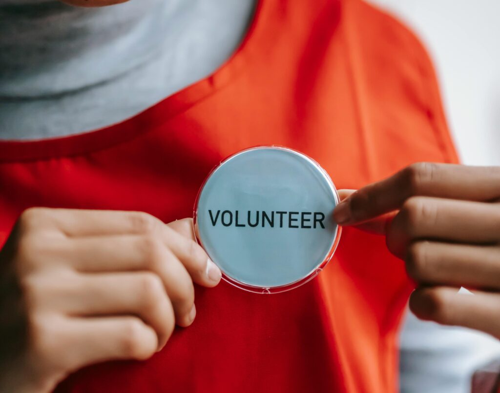 Close-up of a smiling volunteer holding a badge in a bright setting.
